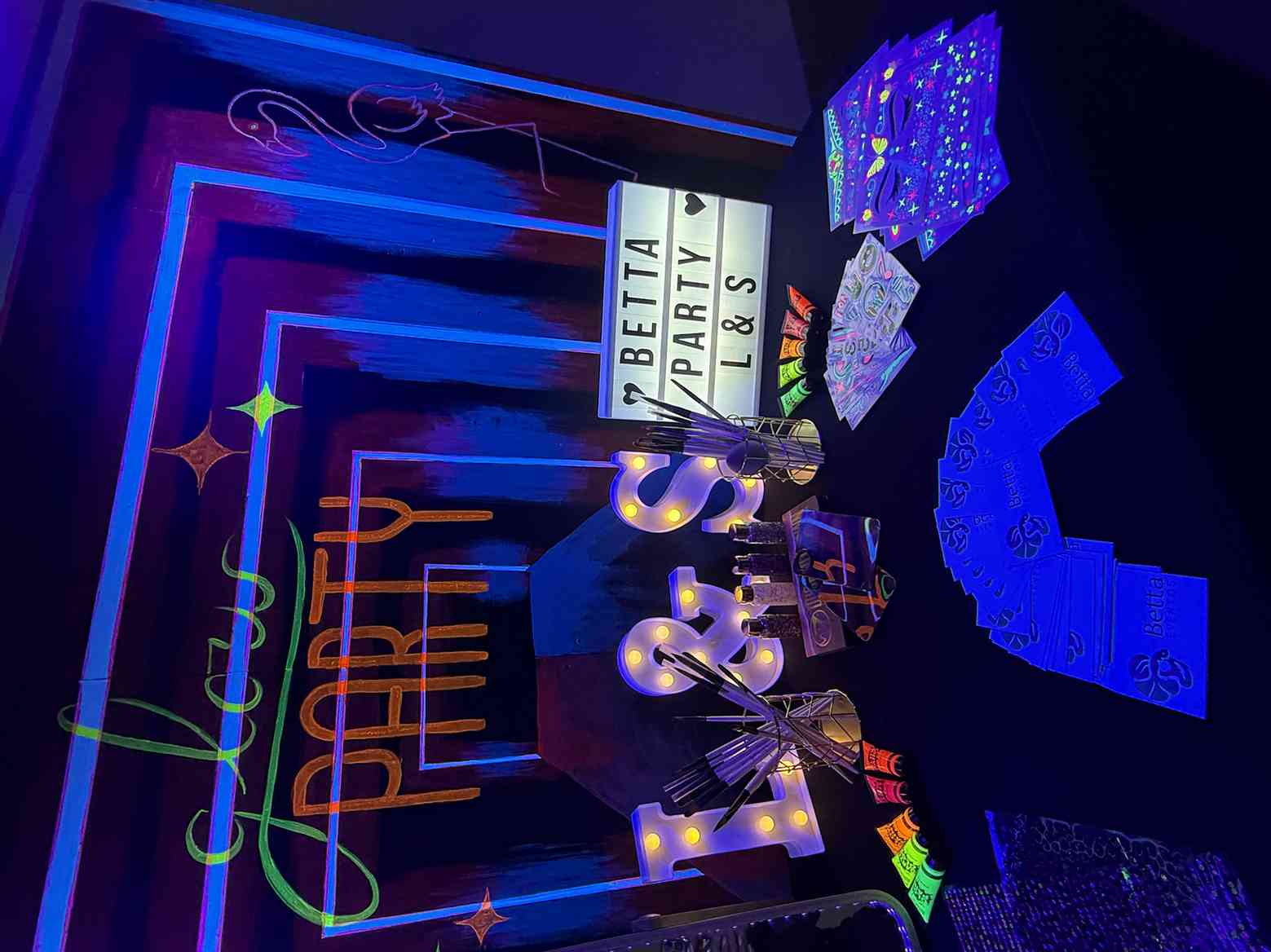 Mesa de manualidades “Glow Party” con letras luminosas y material de purpurina neón