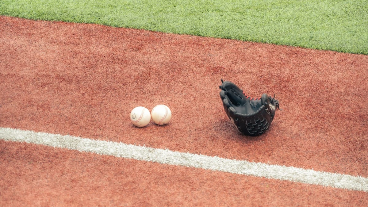 Guante de béisbol y dos pelotas sobre un campo de césped artificial rojo y verde