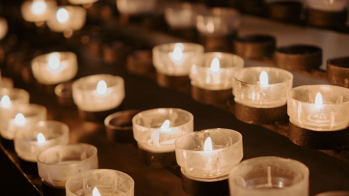Filas de velas encendidas en pequeños vasos de cristal en una iglesia con luz cálida
