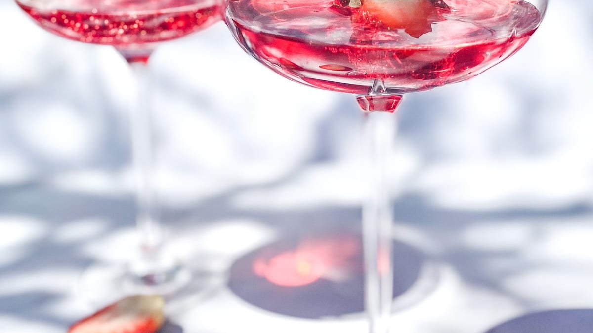 Dos copas de cóctel rosa con fresa sobre una mesa blanca iluminada por el sol