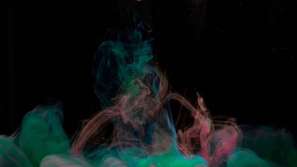 Humo de colores verde y rosa flotando sobre un fondo negro