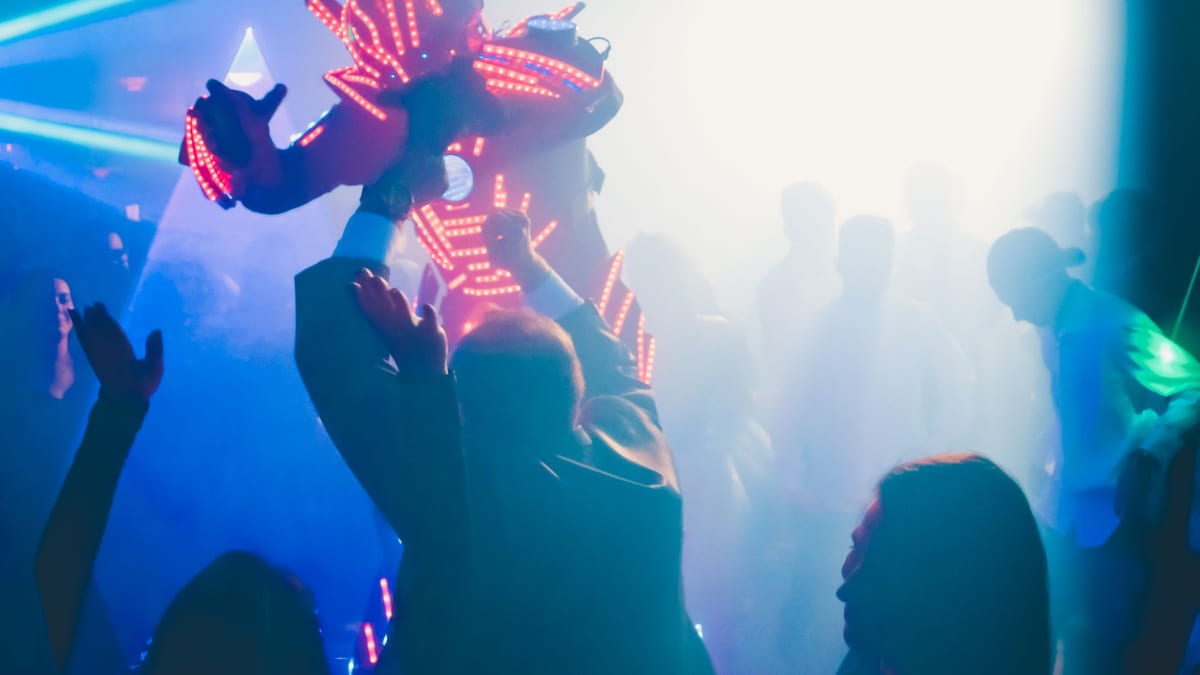 Invitados bailando entre humo y luces de colores, con un artista con traje de luces LED al fondo