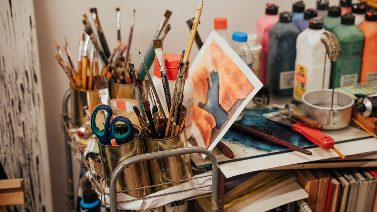 Rincón de taller de arte con pinceles en botes, botellas de pintura y una acuarela apoyada